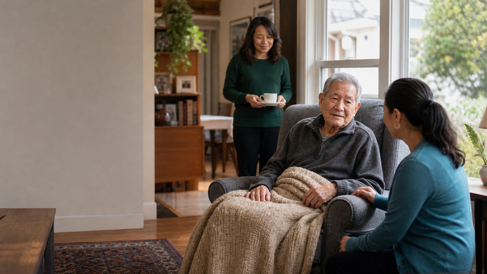 An older man resting comfortably at home with a caregiver and family member nearby